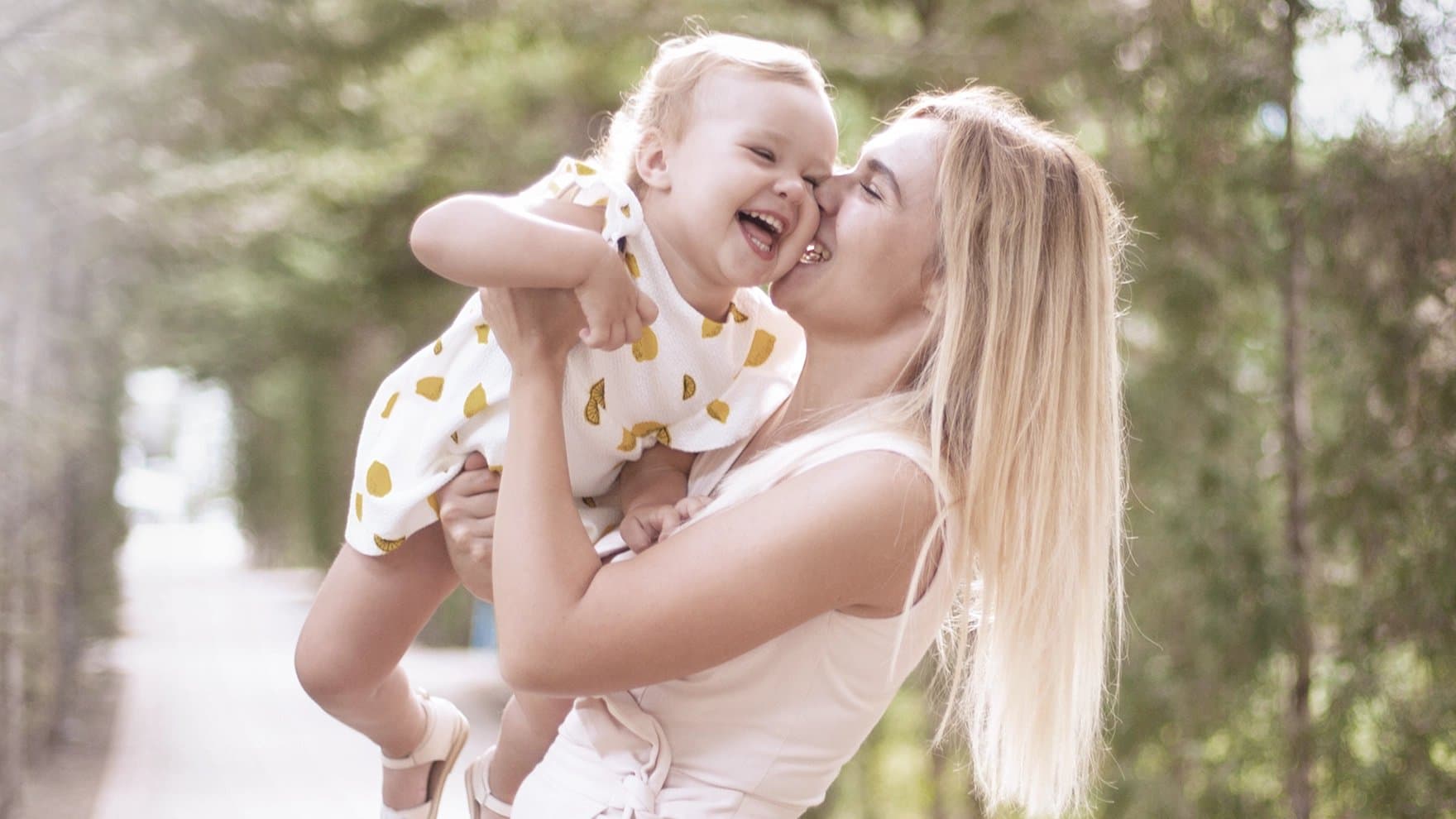 Mutter lacht, während sie ihr Baby hält und es auf die Wange küsst